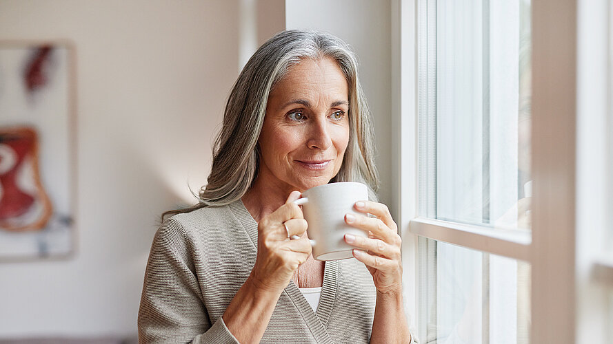 Frau sitzt mit Tasse im Zimmer und träumt 